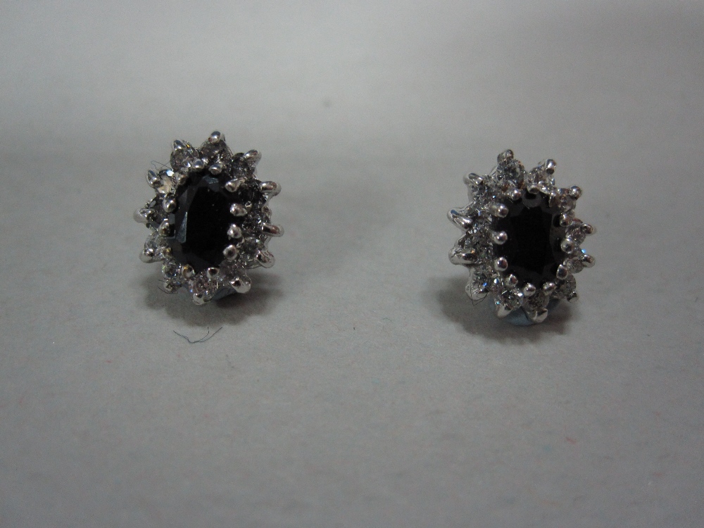 A pair of sapphire and diamond cluster earstuds set in white gold, each with an oval cut navy blue