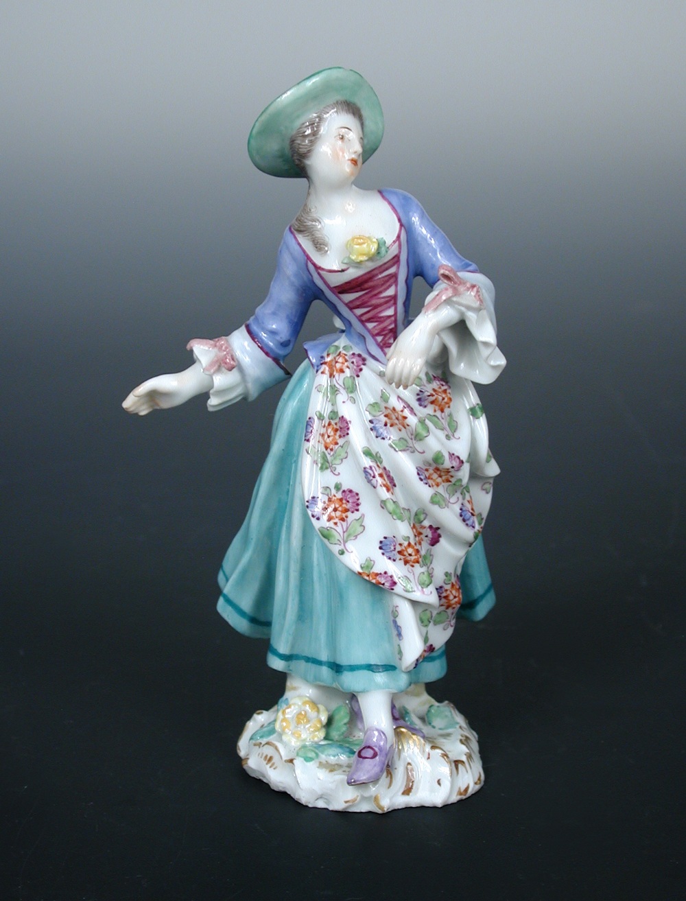 An 18th century Meissen figure of a lady, she wears a floral apron over her pale green dress, her
