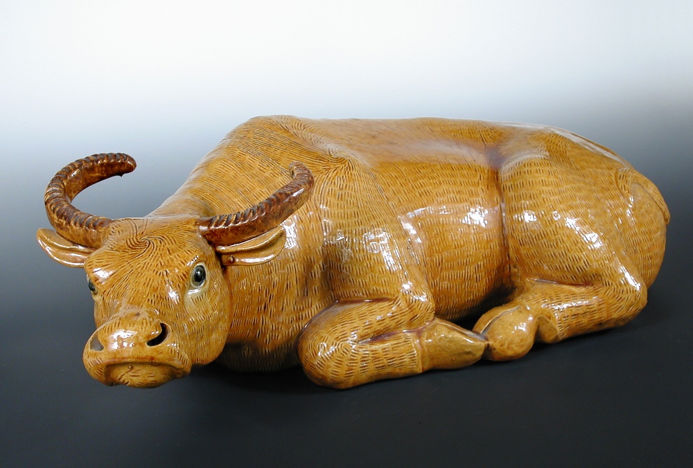 A 19th century Chinese ochre glazed water buffalo, the reclining beast with black eyes and brown