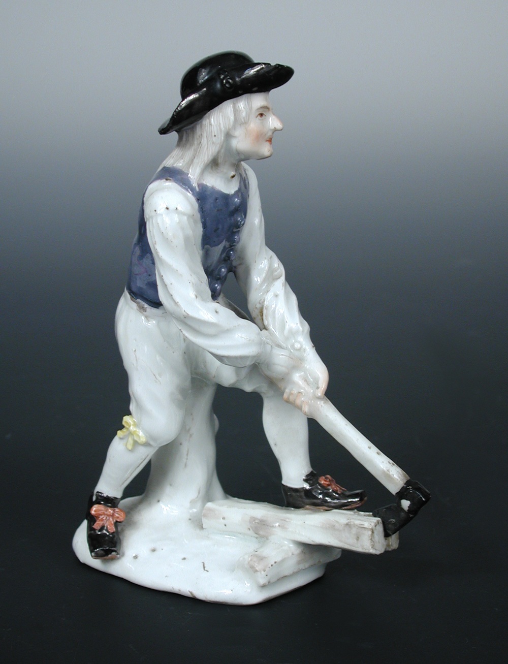 A mid 18th century Meissen figure of a woodcutter after J J Kandler, he wears a black hat and blue