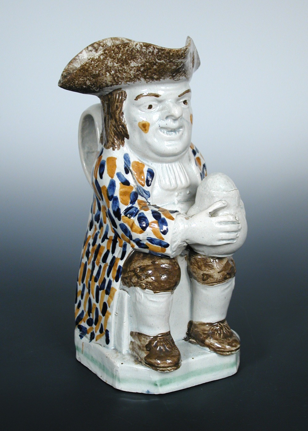 A late 18th/early 19th century Prattware Toby jug, he sits with a foaming mug of ale, his tricorn