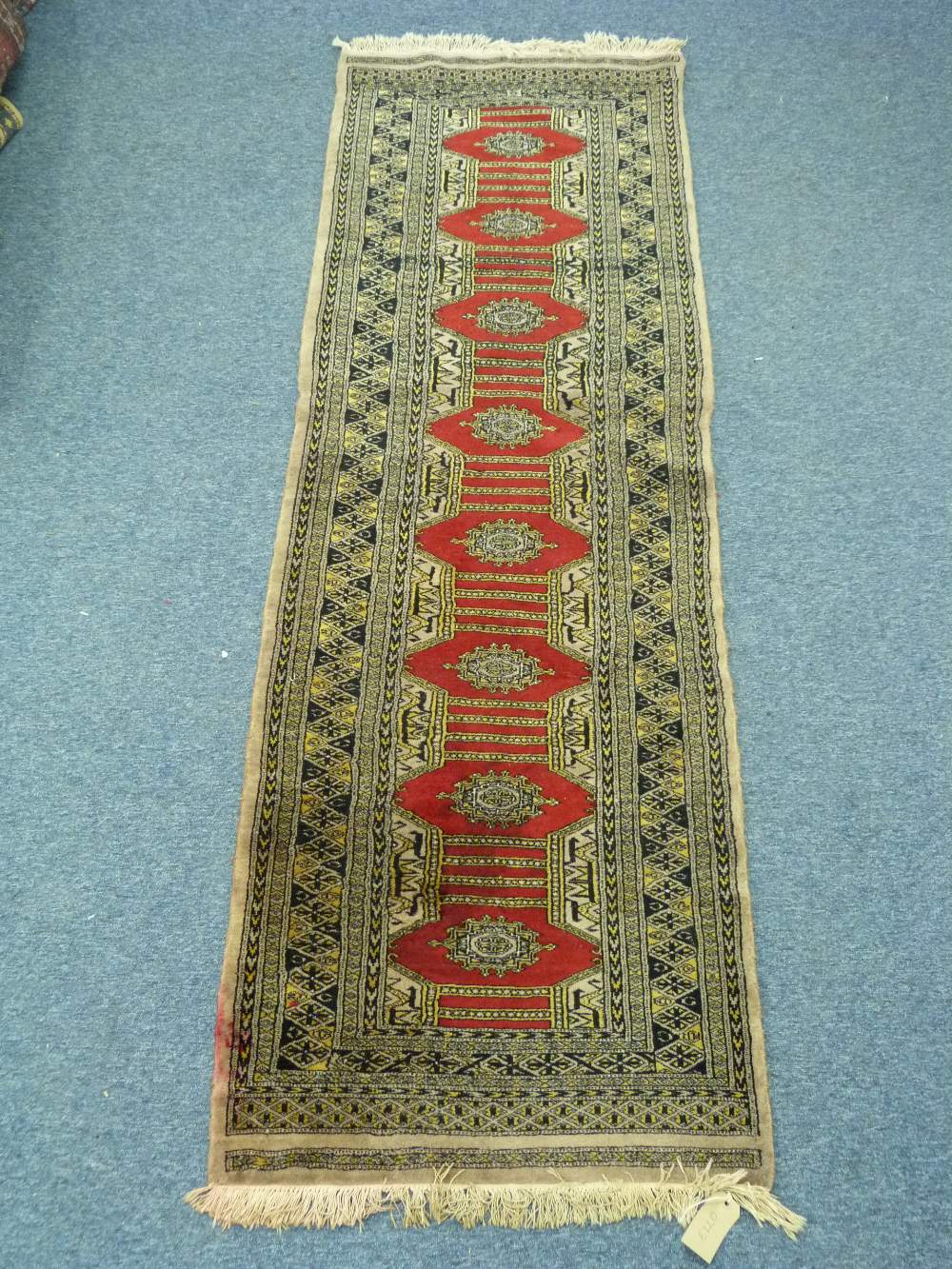Tribal rugs; a runner of red central design on a dark gold ground, 99in x 28in (267cm x 81cm)