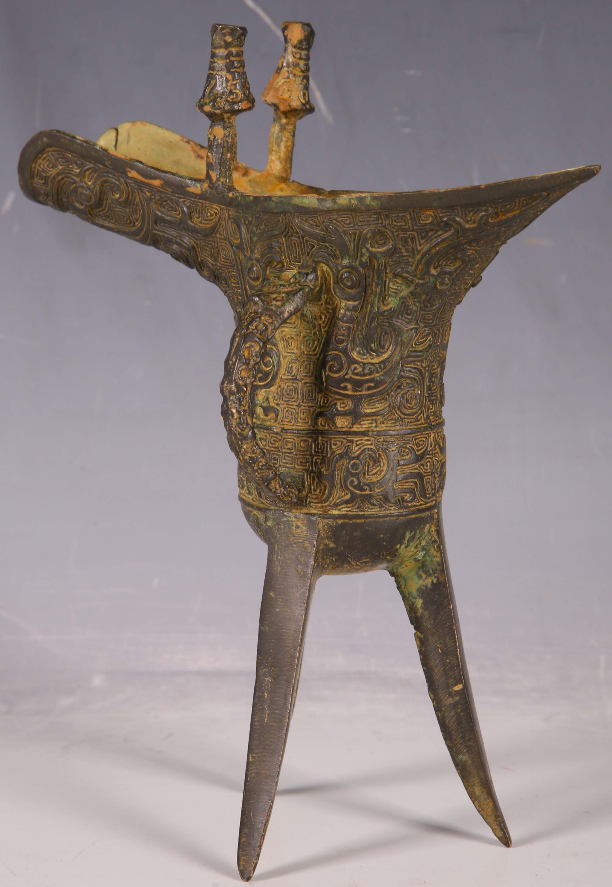 A Chinese bronze, jue wine vessel, twin lugs, mythical beast handle, all over abstract decoration,