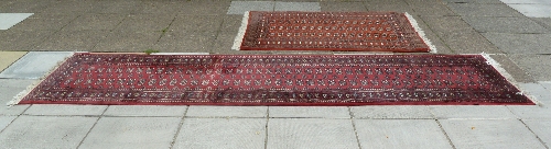 A Bokhara pattern runner, the central crimson ground field of eighty elephant foot medallions, 396cm