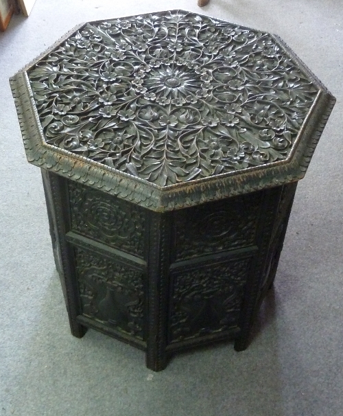 An Indian carved ebonised table, the foliate carved octagonal top on a folding base decorated