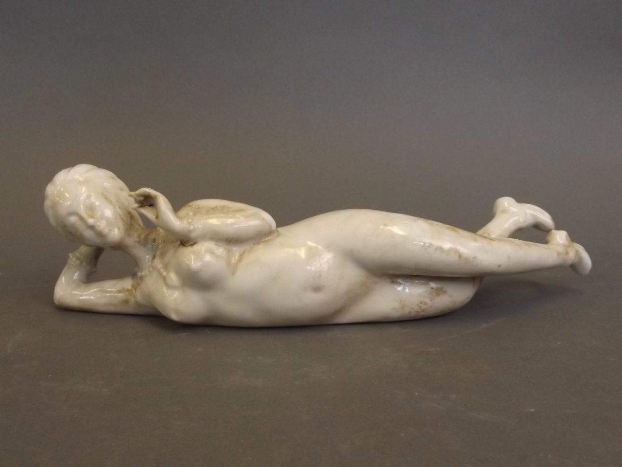 A Chinese white glazed porcelain figure of a reclining nude wearing jewellery, indistinctly marked