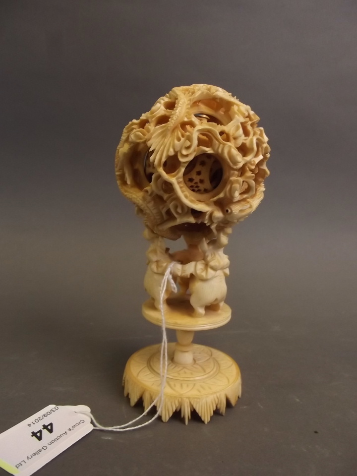 An early C20th Chinese carved ivory puzzle ball decorated with dragons, on an ivory stand, 5½" high