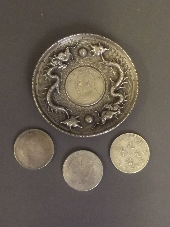 A Chinese silvered metal dish with repousse dragon decoration, and three Chinese coins, dish 4''