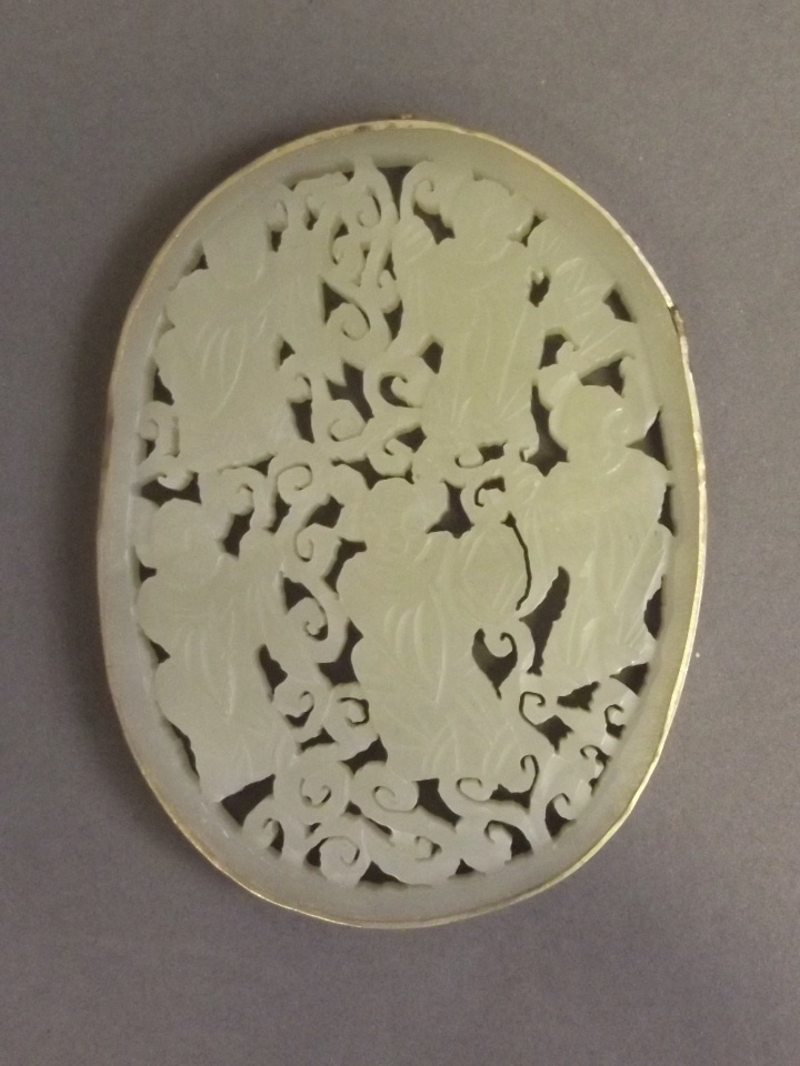 A Chinese pierced and carved celadon jade pendant depicting the Five Sages, in a silvered metal
