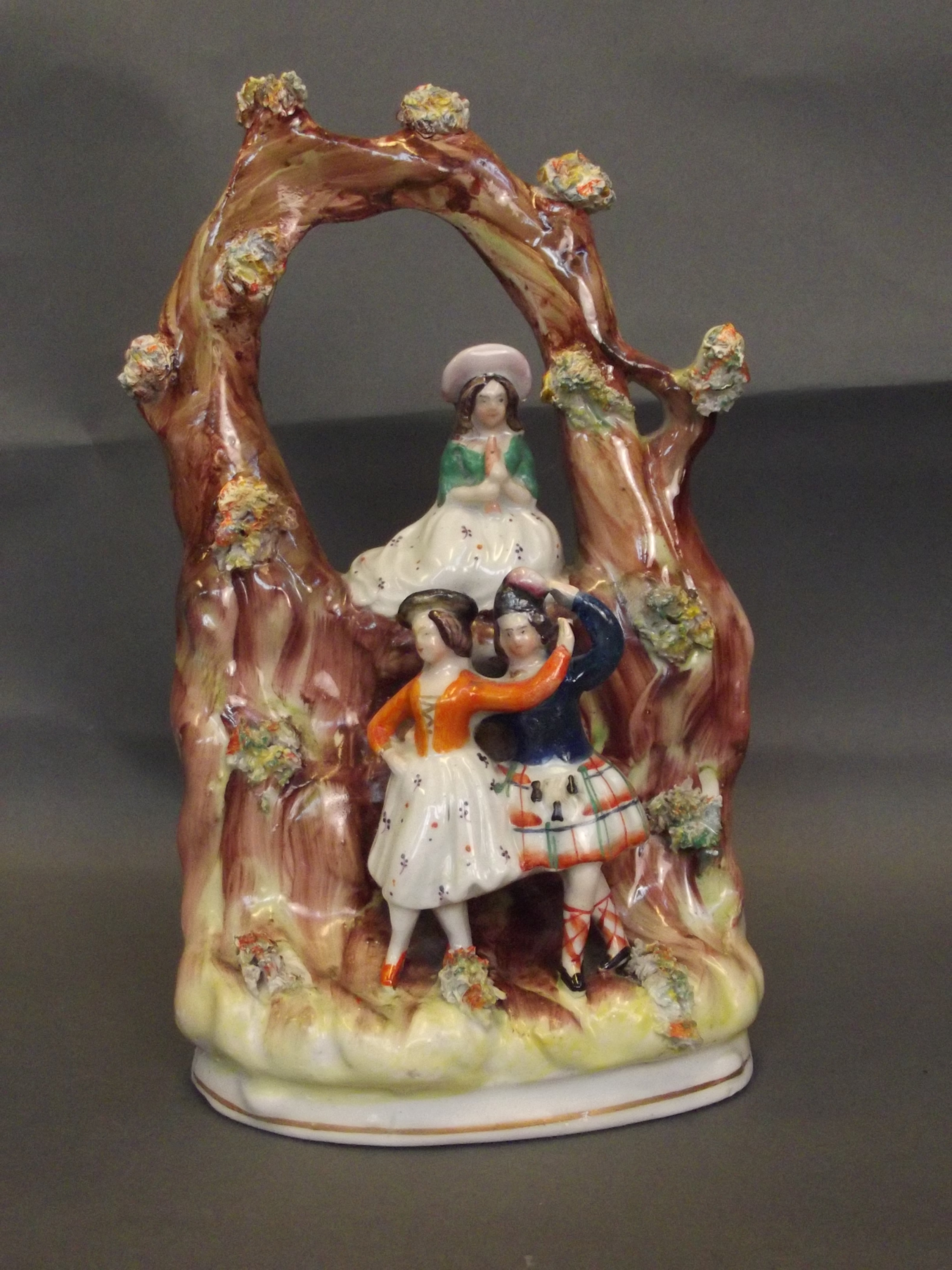 A C19th Staffordshire Arbour group depicting two dancers below a seated girl playing a flute,