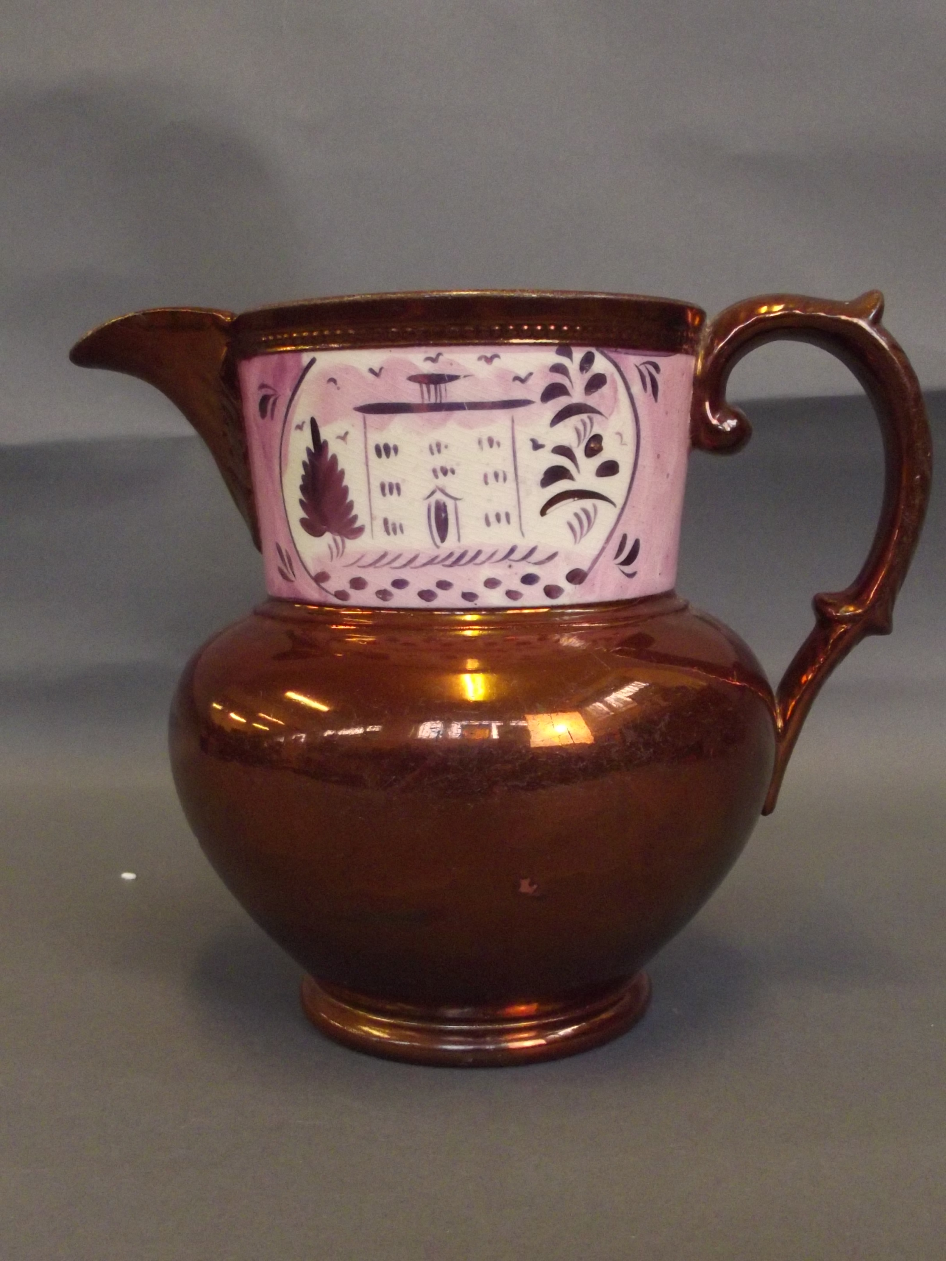 A C19th copper lustre jug with a pink lustre border to top depicting a house amongst trees, 6''