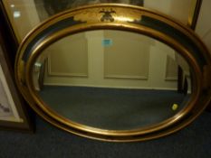 An oval bevelled edge wall mirror in gilt and dark green frame