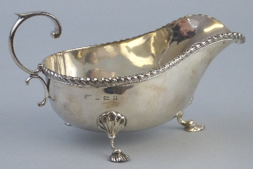 An Edwardian sauce boat, with gadrooned rim and flying scroll loop handle raised on shell capped