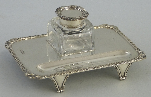 A late Victorian ink stand, of rounded oblong form, the gadrooned rim with scrolling leaf applied