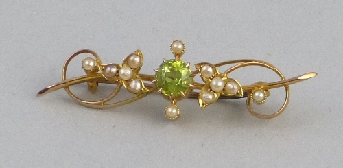 A peridot and seed pearl bar brooch, comprising a central circular peridot set on 15ct gold wire