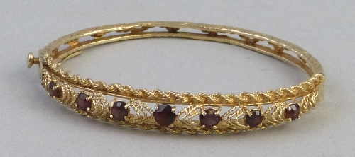 A 14k gold bangle, of pierced form, the top section set with graduated garnets within a rope twist