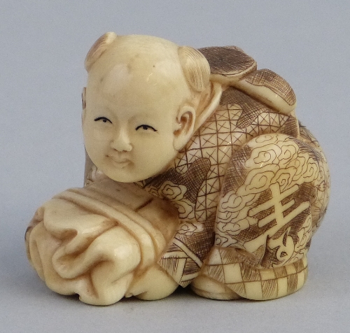 A Japanese ivory okimono figure, carved as a young boy crouching holding a tied bundle, signed, 4.