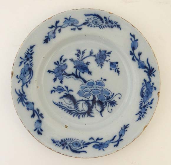 An 18thC Delft plate painted in blue with Chinoiserie floral design with trailing foliate sprays