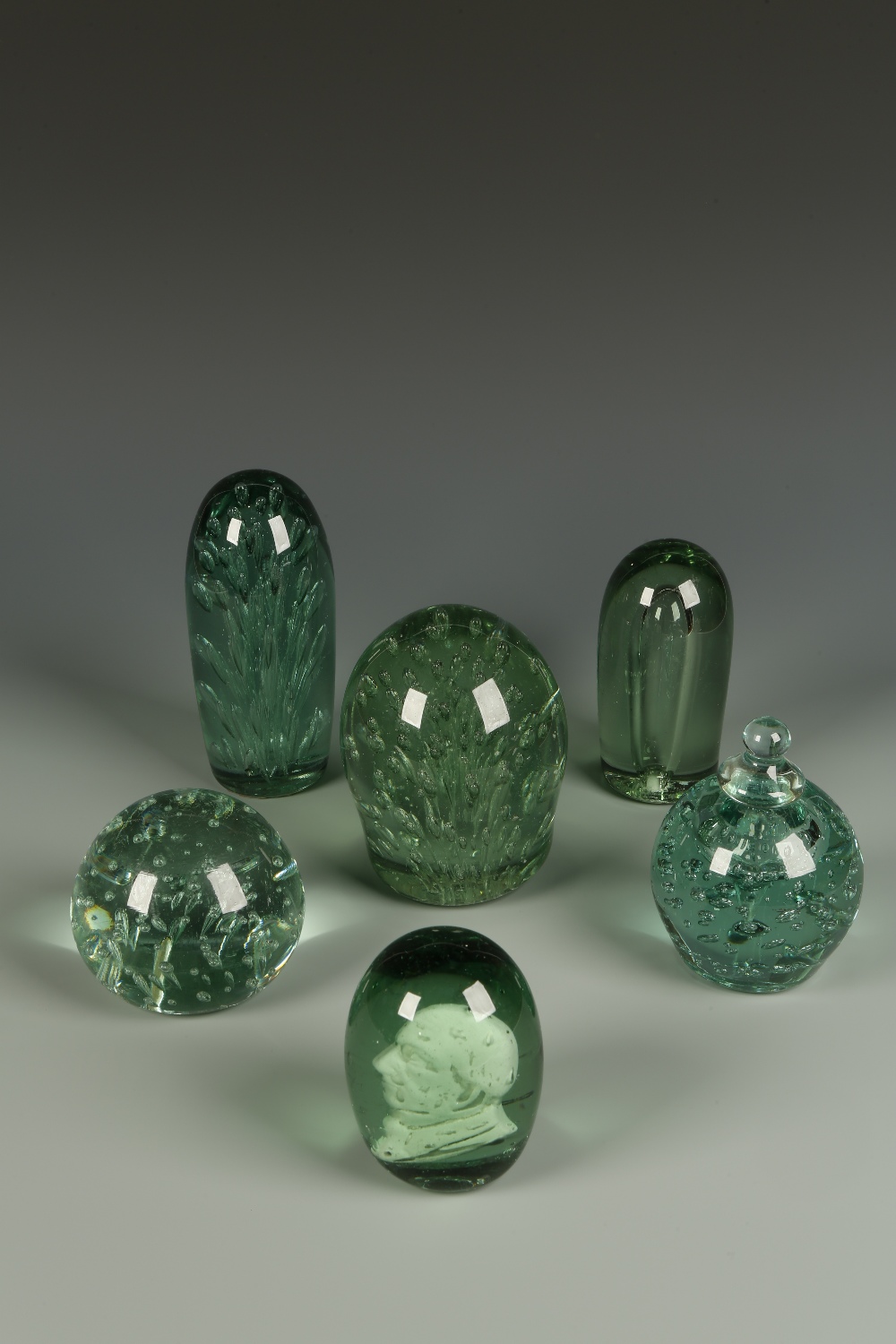 A PALE GREEN GLASS ""DUMP""-TYPE PAPERWEIGHT with tiered bubble inclusions and three similar