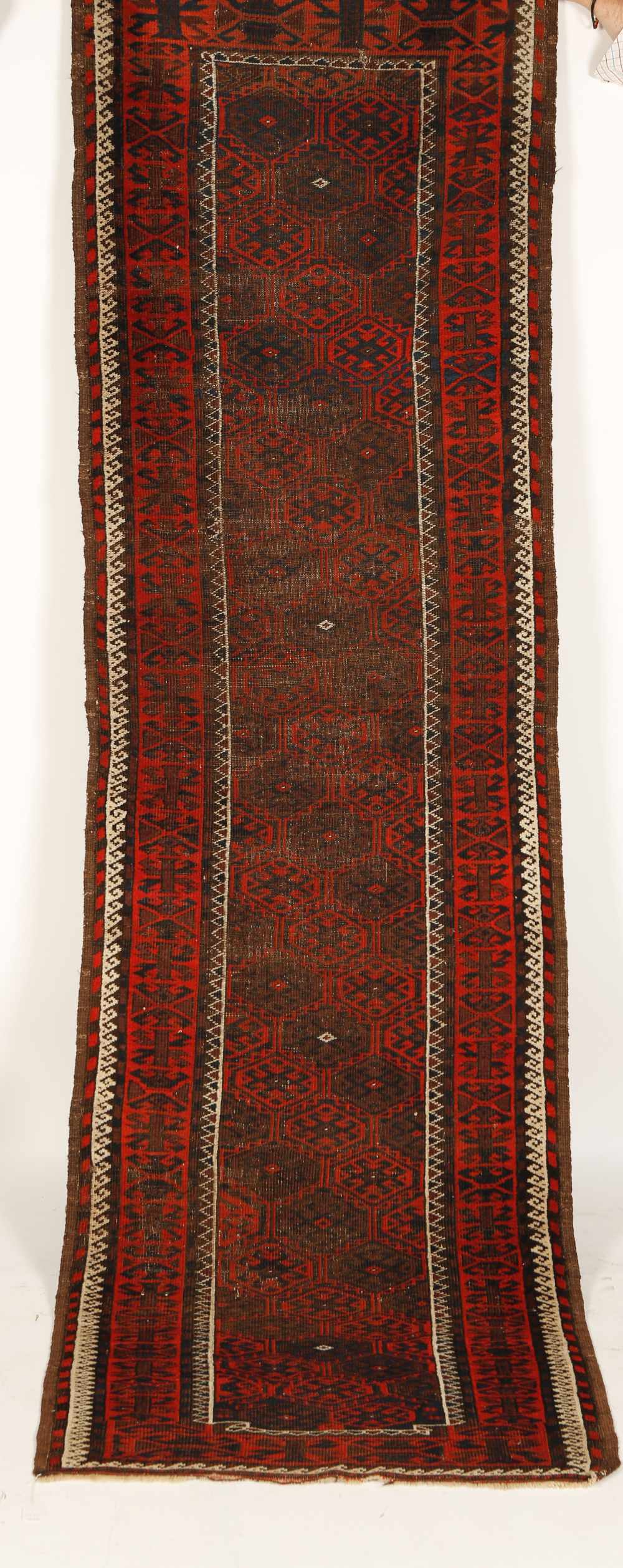 A TEKKE TYPE RUNNER worked with repeating hexagonal motifs in red and brown against a dark ground