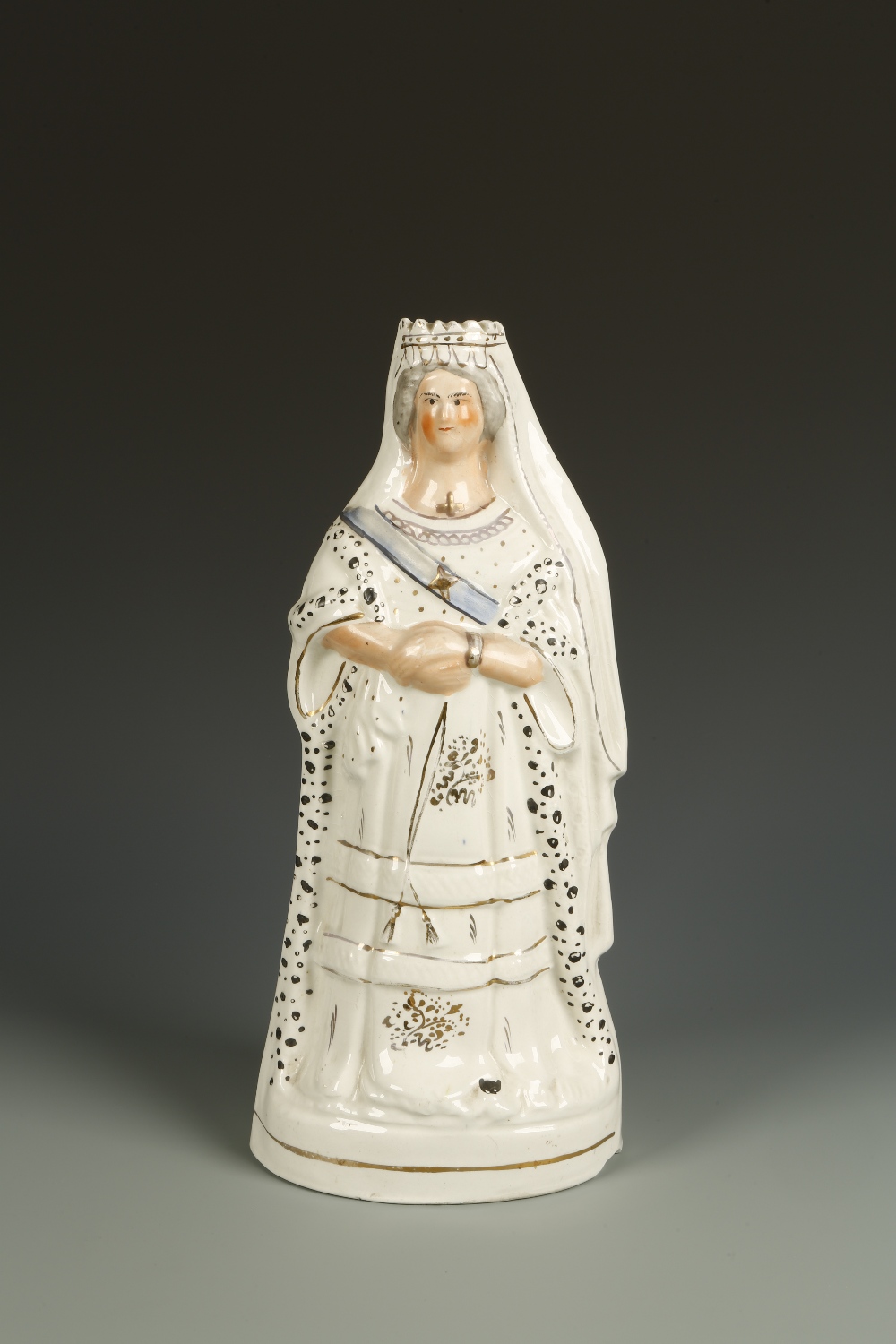 A STAFFORDSHIRE PORTRAIT FIGURE OF QUEEN VICTORIA standing with arms folded wearing a gilt