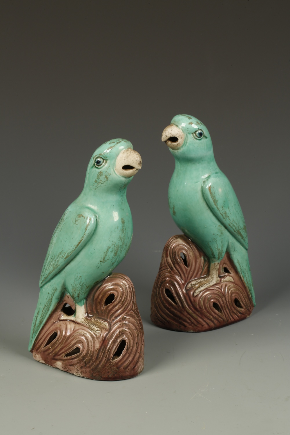 A PAIR OF CHINESE BISCUIT-GLAZED BIRDS, each with its` head raised and standing on rocks, Qing, 8.