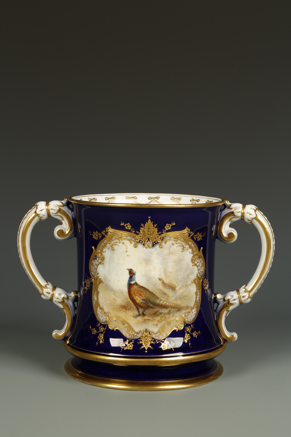 A ROYAL WORCESTER TWO HANDLED CUP painted with a cartouche of pheasants, signed ""James Stinton""