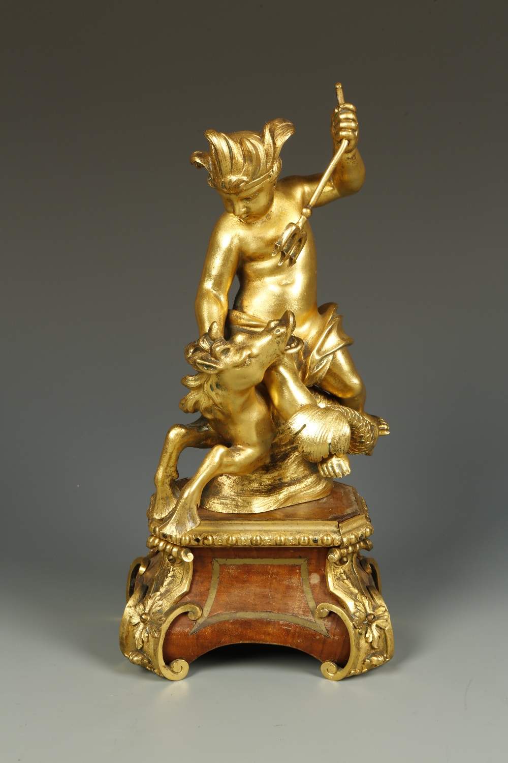 A GILT BRONZE OF A YOUTHFUL NEPTUNE with a trident aloft riding on the back of a hippocamp, on an