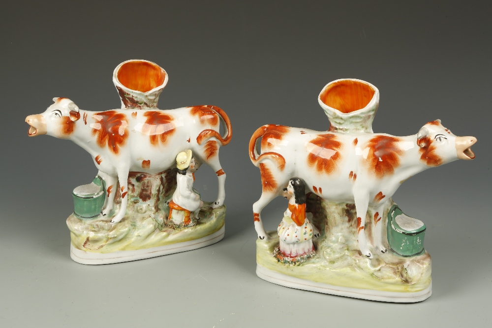 A PAIR OF STAFFORDSHIRE POTTERY COW SPILL VASE ORNAMENTS, each decorated with a cow being milked by