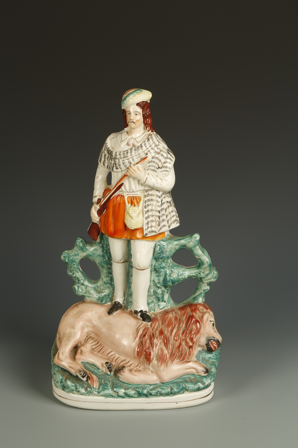 A STAFFORDSHIRE FLAT-BACK FIGURE OF A HUNTSMAN standing over a slain lion, with green bocage to the