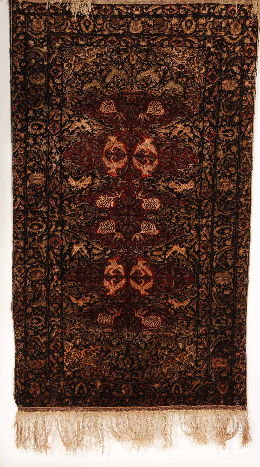 A PERSIAN SILK RUG worked with stylised foliate motifs in red and silver against a black ground