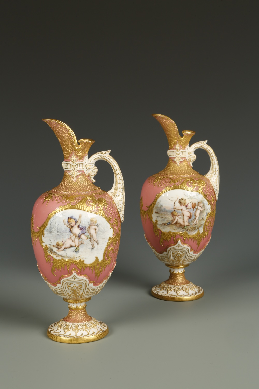 A PAIR OF ROYAL WORCESTER PORCELAIN EWERS painted with cartouche-shaped panels of cherubs ice-