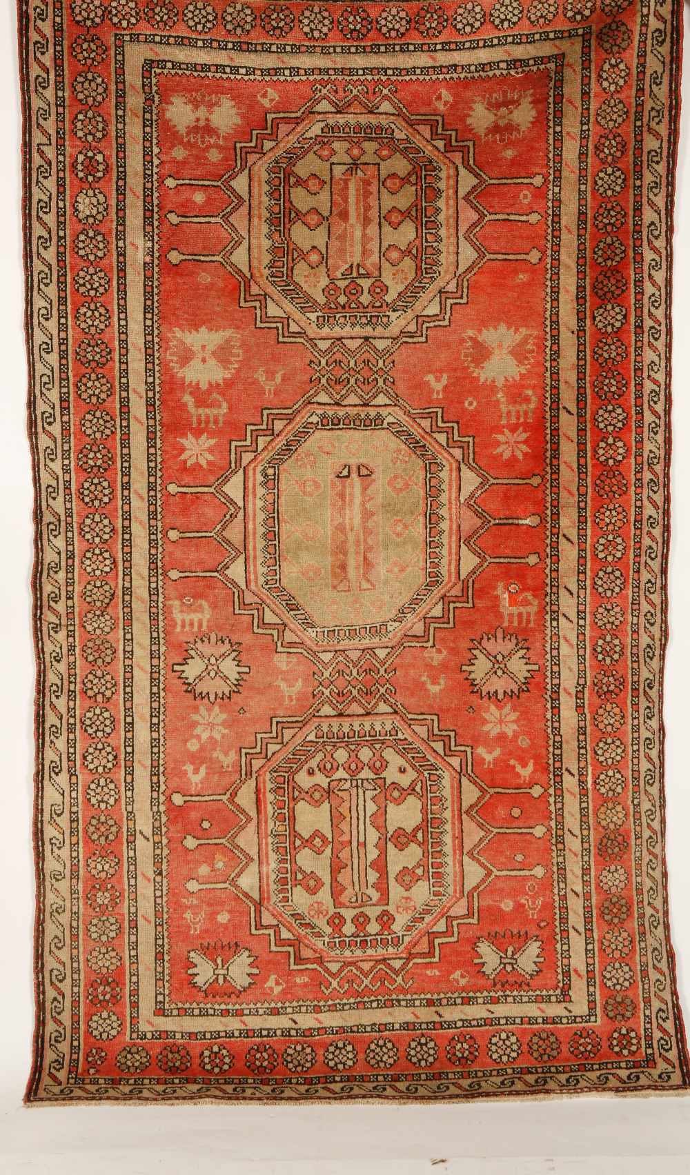 A CAUCASIAN RUG worked with three broad central medallions against a pale red ground with stylised