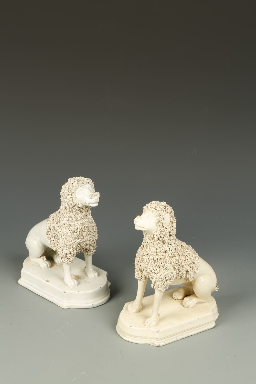 TWO SIMILAR EARLY STAFFORDSHIRE MODELS OF POODLES, each with clipped coats, seated on plinth bases,