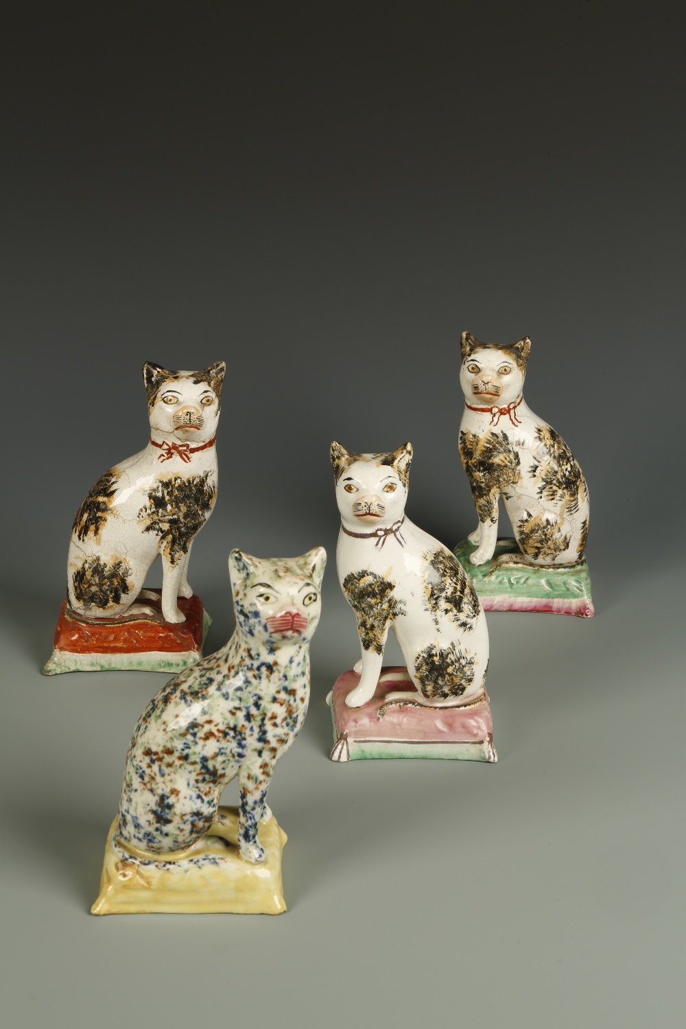 A NEAR PAIR OF STAFFORDSHIRE CAT FIGURES, each with sponged tabby fur, seated on cushions, and a