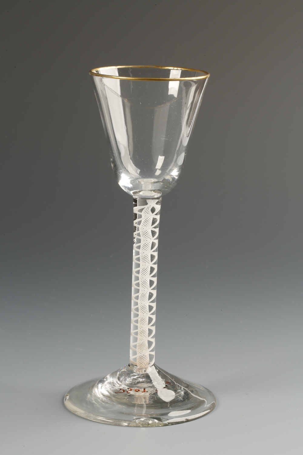 AN 18TH CENTURY SMALL WINE GLASS with a plain tapering bowl with gilt rim, on a spiral gauze air-