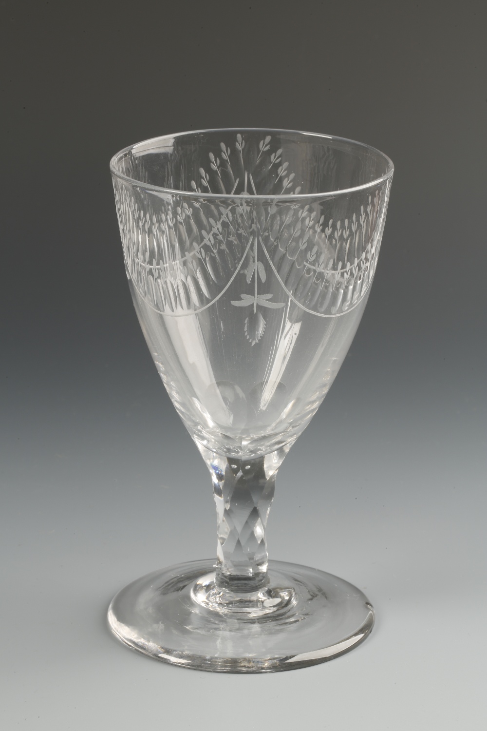 A GEORGE III STYLE WINE GLASS with a broad deep bowl with engraved swag decoration, on a faceted
