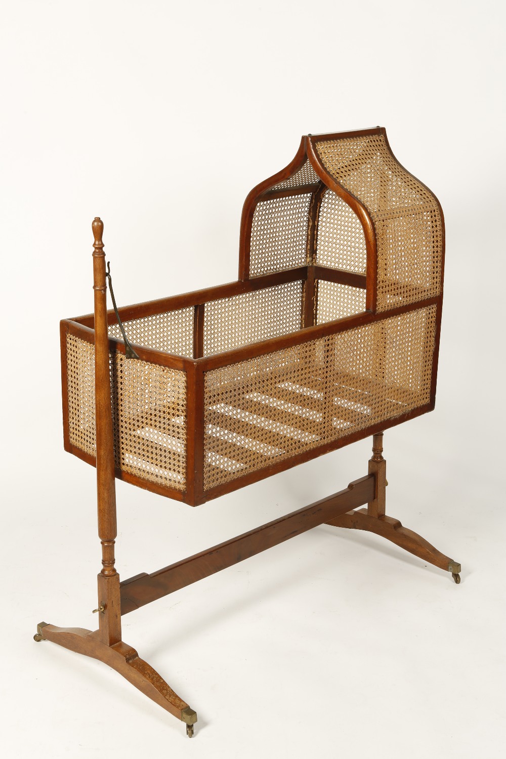 A REGENCY MAHOGANY ROCKING CRADLE with a cane-work cradle on turned uprights and downswept legs with