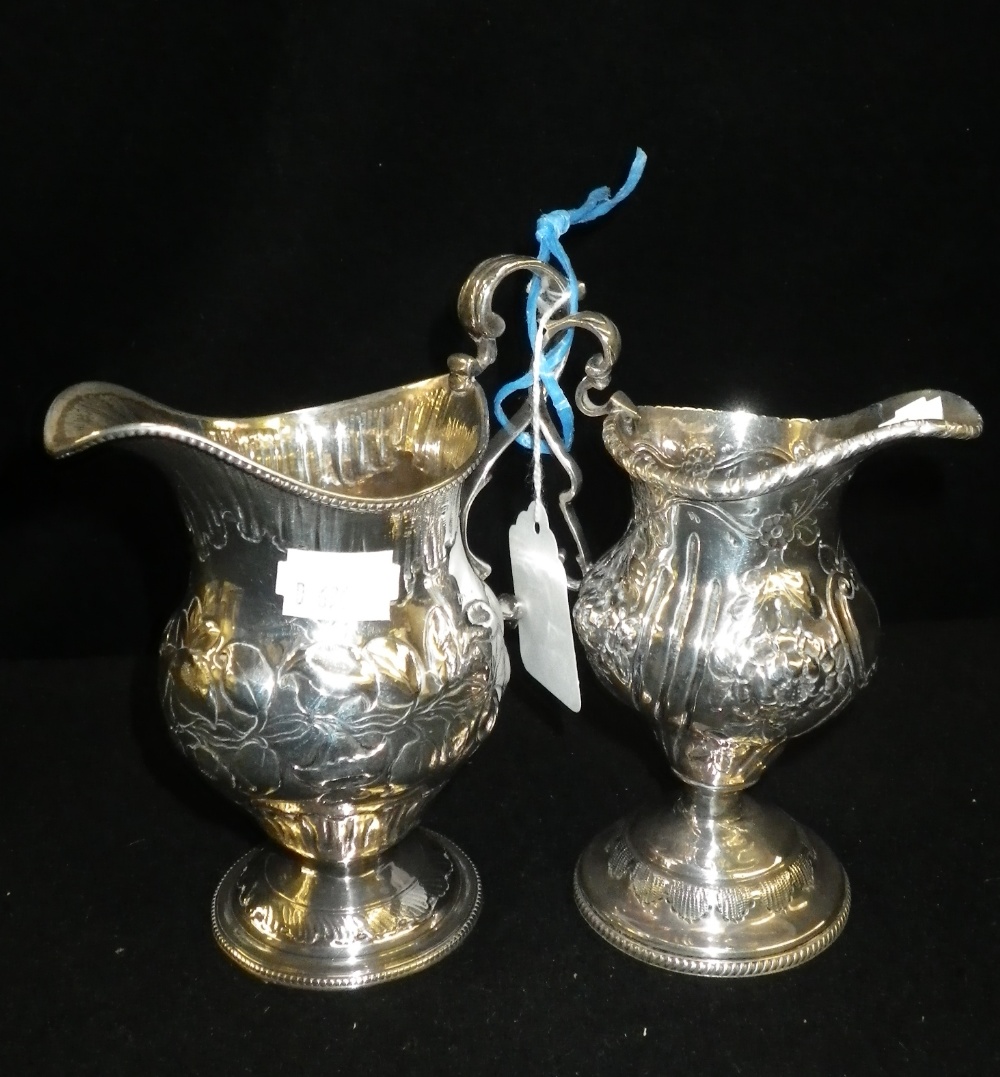 A baluster-shaped repoussé decorated silver cream jug and a similar smaller example (2)