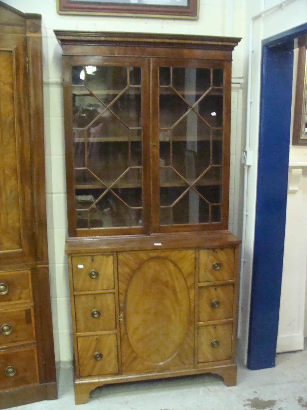 A Regency mahogany library cabinet with glazed upper section, the cabinet with central oval