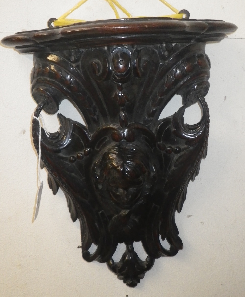 A carved oak wall bracket, decorated with scrolling foliage and the head of a girl