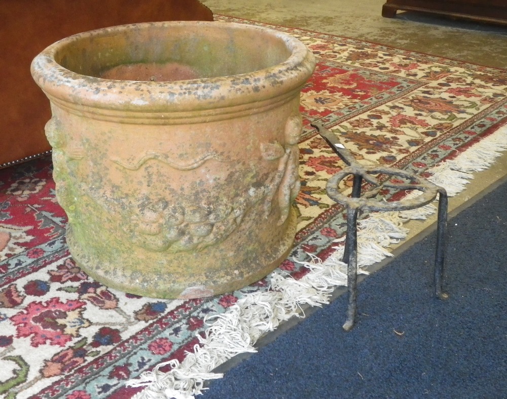 A terracotta garden planter decorated with floral swags and cherubs and an iron trivet.