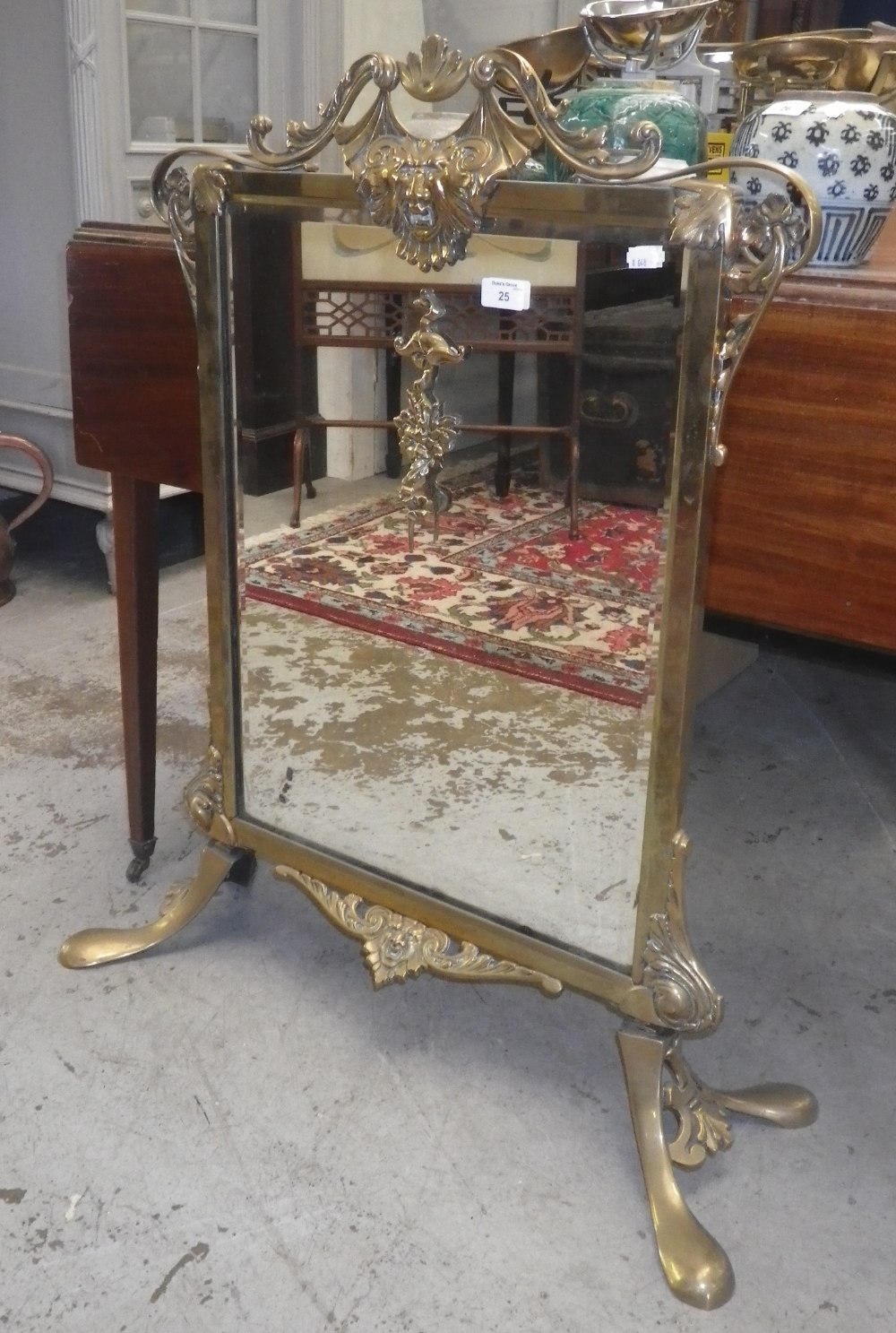 An Edwardian brass framed mirrored fire-screen with mask decoration.