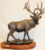 A large bronze effect cast iron statue of a stag. Standing proud with large horns, on a wooden