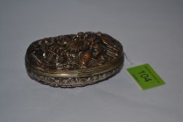 A silver white metal over bronze pill box being oval in shape with lid in relief of game and garden