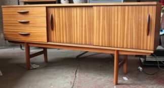 A retro 1970`s teak sideboard of small proportions being raised on turned legs with sliding door