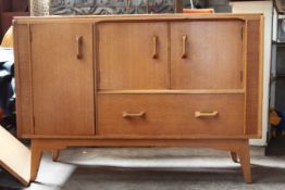 A vintage 1950`s Ernest Gomme G-Plan oak sideboard being raised on angular tapered feet with