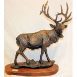 A large bronze effect cast iron statue of a stag. Standing proud with large horns, on a wooden
