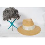 A 1970's green plastic wig stand together with wig and a straw hat