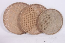 A series of graduated whicker trays of circular form being handwoven.  6cm x 70cm